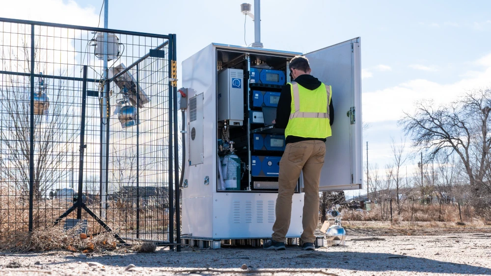 Environmental technician inspecting air monitoring equipment at an outdoor industrial site.