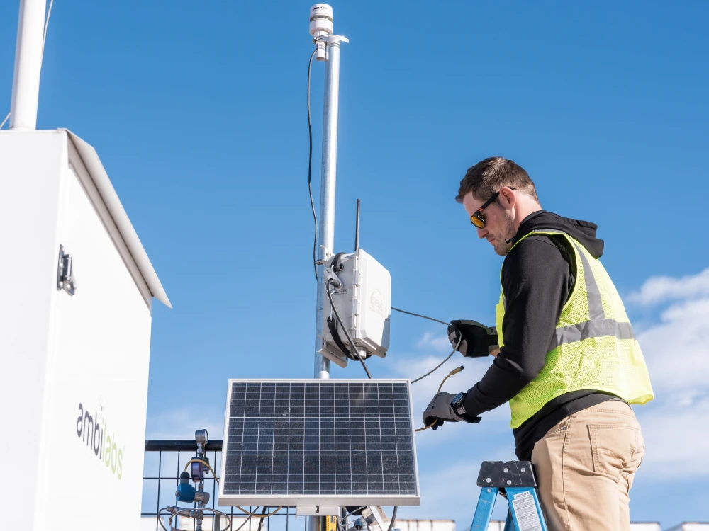 Field technician servicing solar-powered environmental monitoring equipment outdoors.