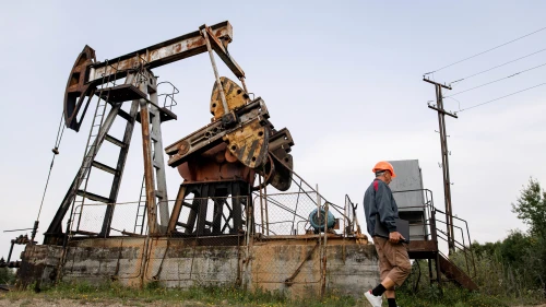 Worker wearing PPE walking near an oil pumpjack in an onshore oil field.