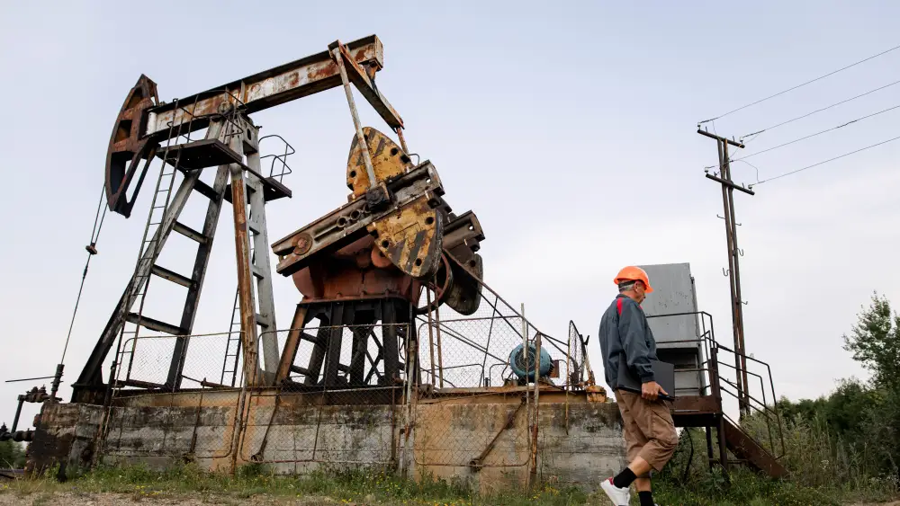 Worker wearing PPE walking near an oil pumpjack in an onshore oil field.