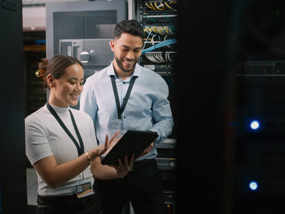 Two professionals reviewing data on a tablet inside a server room