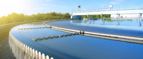 Circular clarifier tank at a wastewater treatment facility with clean water and mechanical equipment under clear sky.