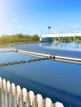 Circular clarifier tank at a wastewater treatment facility with clean water and mechanical equipment under clear sky.