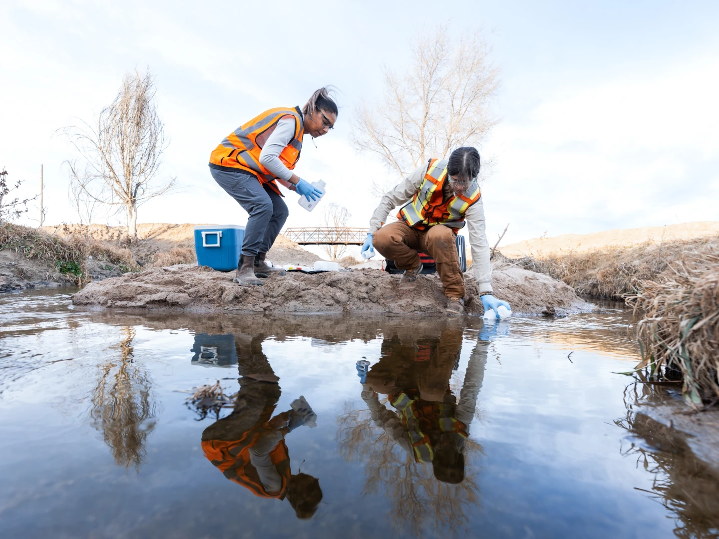 Two employees wearing ppe taking water samples in the field-on site sampling.