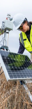 Field technician servicing solar-powered environmental monitoring equipment in a remote outdoor location