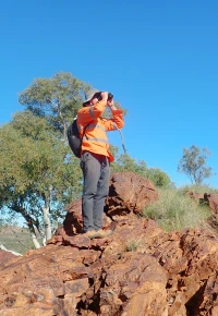 Field worker surveying rocky terrain with binoculars.
