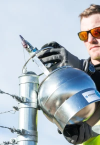 An employee inspecting industrial equipment near a barbed wire fence.