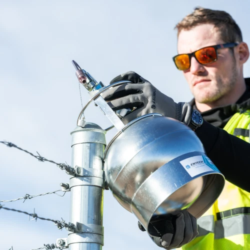 An employee inspecting industrial equipment near a barbed wire fence.
