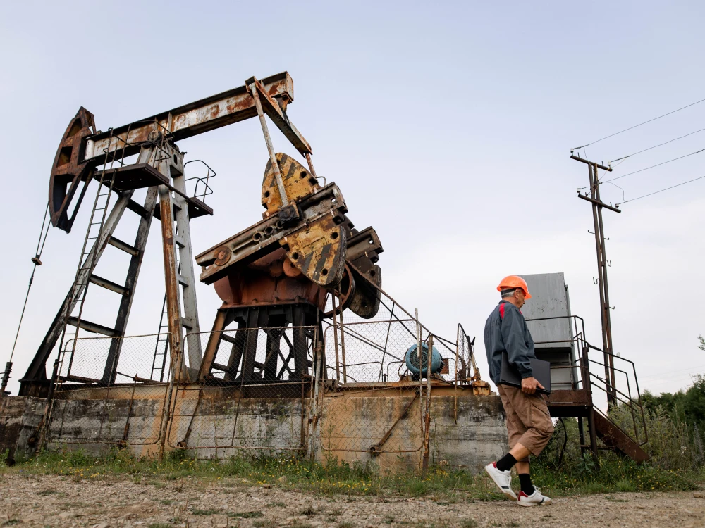Worker wearing PPE walking near an oil pumpjack in an onshore oil field.