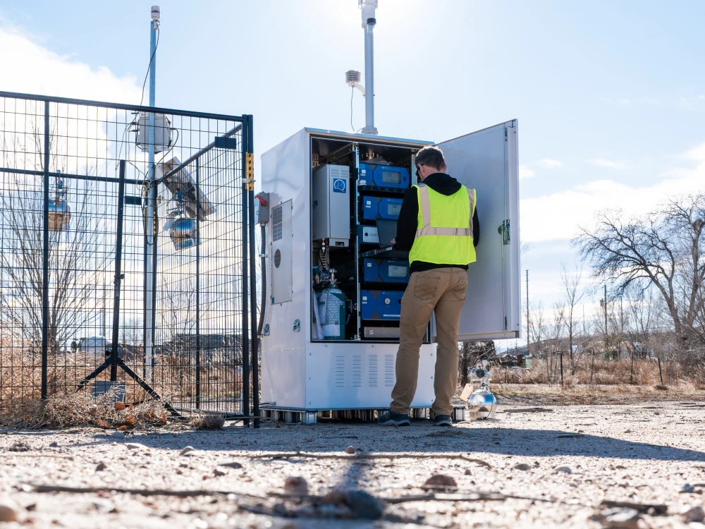 Environmental technician inspecting air monitoring equipment at an outdoor industrial site.