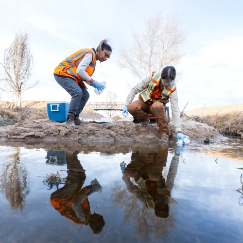Two employees wearing ppe taking water samples in the field-on site sampling.