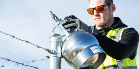An employee inspecting industrial equipment near a barbed wire fence.