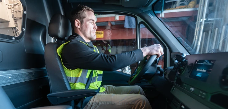 Employee in safety vest driving inside truck