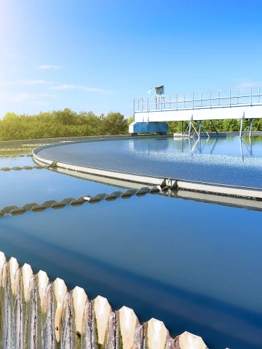 Circular clarifier tank at a wastewater treatment facility with clean water and mechanical equipment under clear sky.