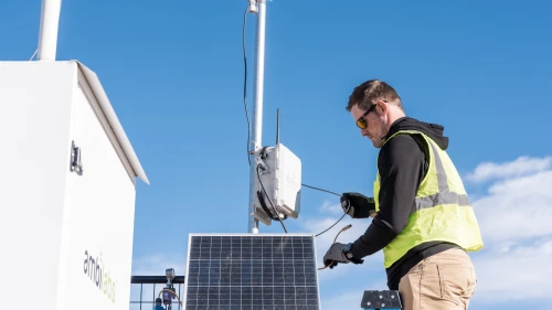 Field technician servicing solar-powered environmental monitoring equipment outdoors.
