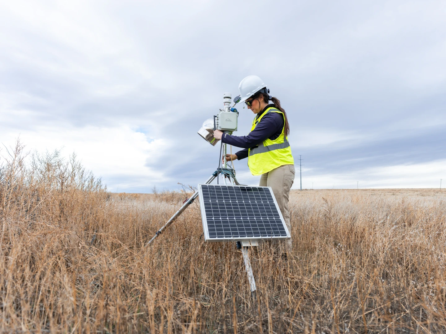 Field technician operating solar-powered environmental monitoring equipment in a grassland setting.