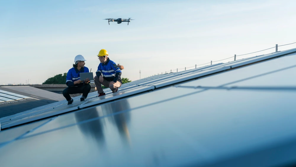 Technicians inspecting solar panels on a rooftop while a drone flies overhead