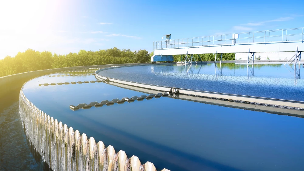 Circular clarifier tank at a wastewater treatment facility with clean water and mechanical equipment under clear sky.