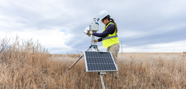 Field technician operating solar-powered environmental monitoring equipment in a grassland setting.