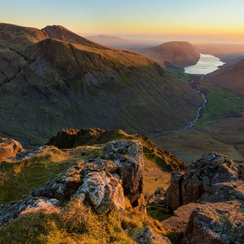 Scenic view of a mountain valley with a winding river leading to a distant lake under warm sunset light.