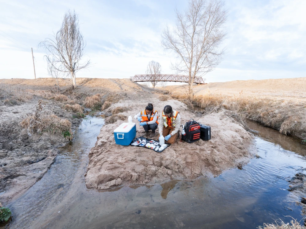 Employees collecting water samples in a stream.
