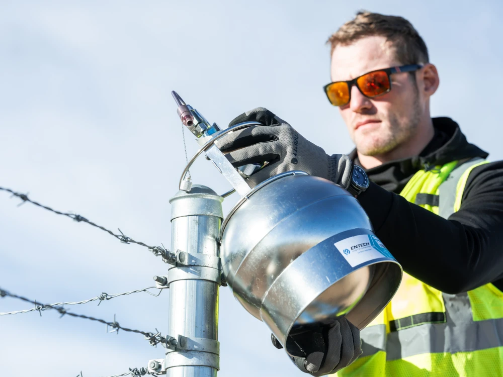 An employee inspecting industrial equipment near a barbed wire fence.