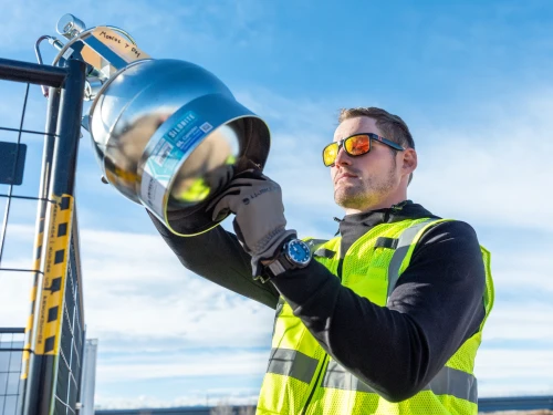 An employee in a safety vest inspecting industrial equipment outdoors.