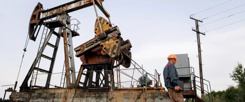 Worker wearing PPE walking near an oil pumpjack in an onshore oil field.