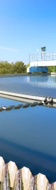 Circular clarifier tank at a wastewater treatment facility with clean water and mechanical equipment under clear sky.
