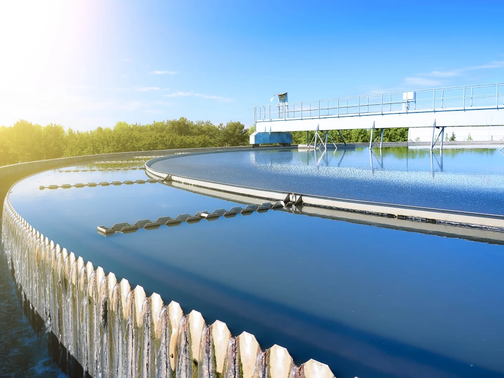 Circular clarifier tank at a wastewater treatment facility with clean water and mechanical equipment under clear sky.