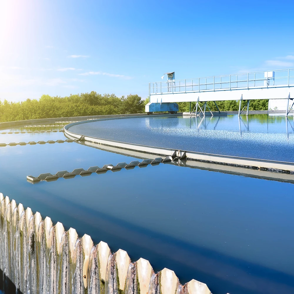 Circular clarifier tank at a wastewater treatment facility with clean water and mechanical equipment under clear sky.