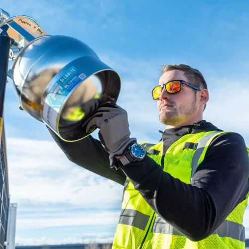 An employee in a safety vest inspecting industrial equipment outdoors.