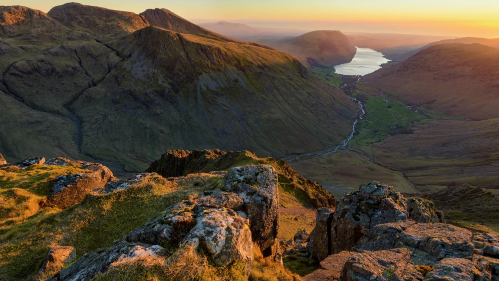 Scenic view of a mountain valley with a winding river leading to a distant lake under warm sunset light.